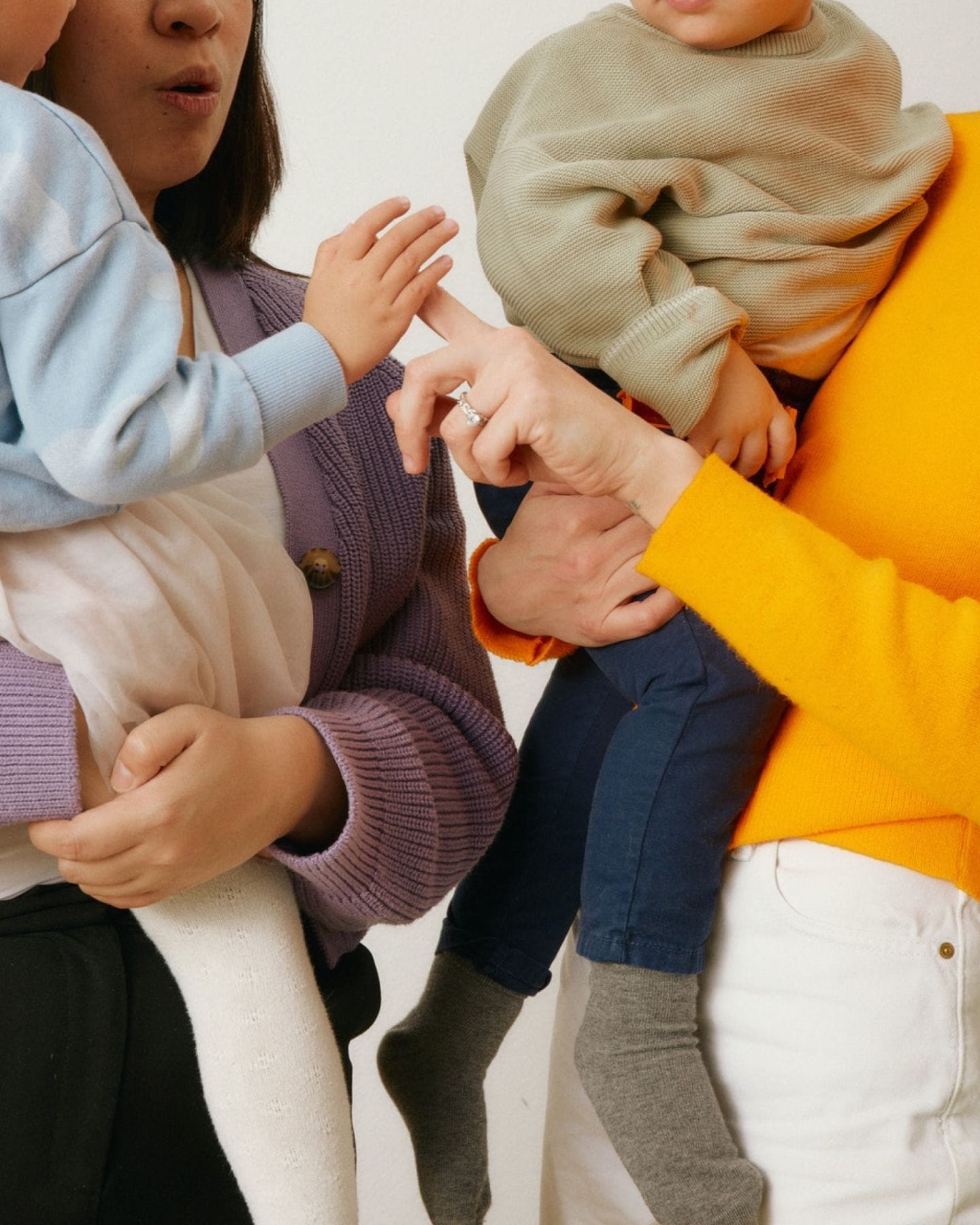 A close-in shot of two adults holding children on their hips, touching hands.