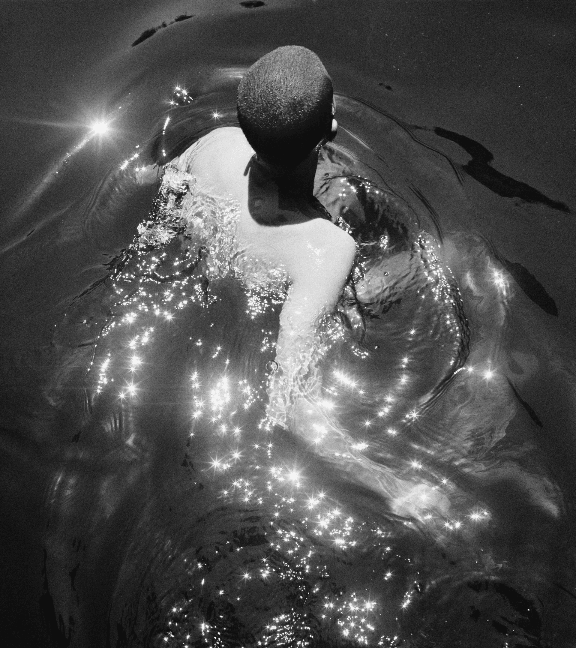 A black-and-white photo of a person swimming through a glistening pool of water.
