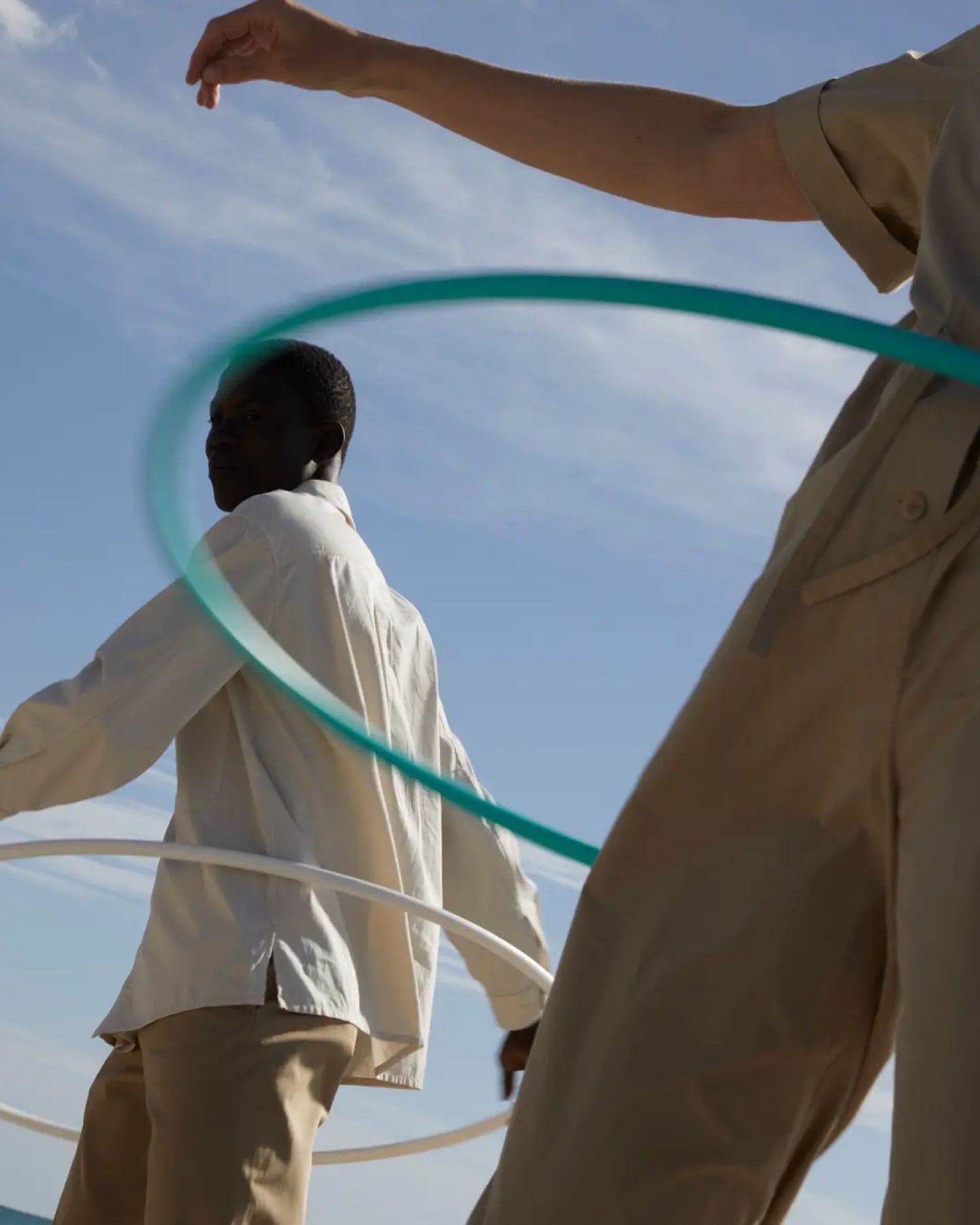 Two people in white shirts and khakis hula-hooping against a blue sky.