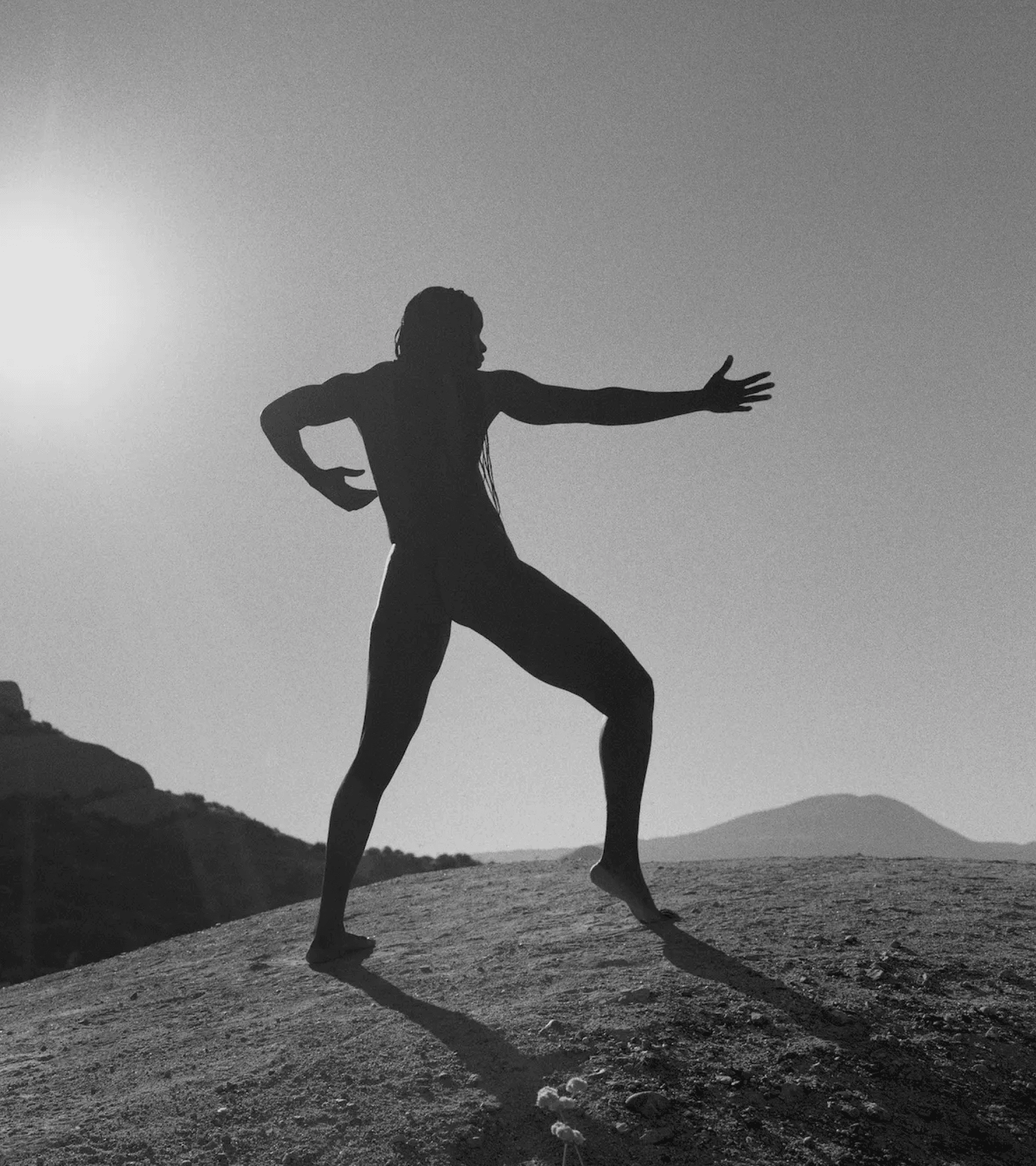 A person dancing on a barren landscape, backlit by the sun in a cloudless sky.