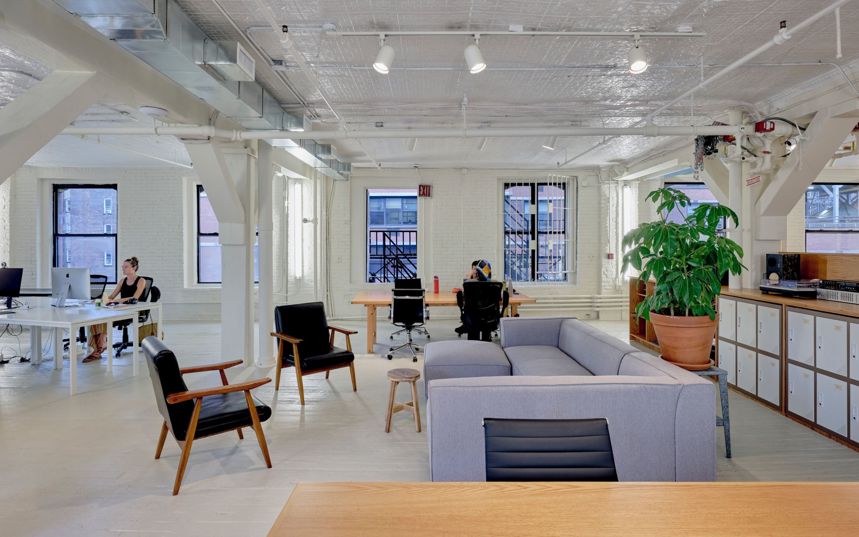 Index NYC studio lounge area with sofas, armchairs, plants, and exposed timber beams.