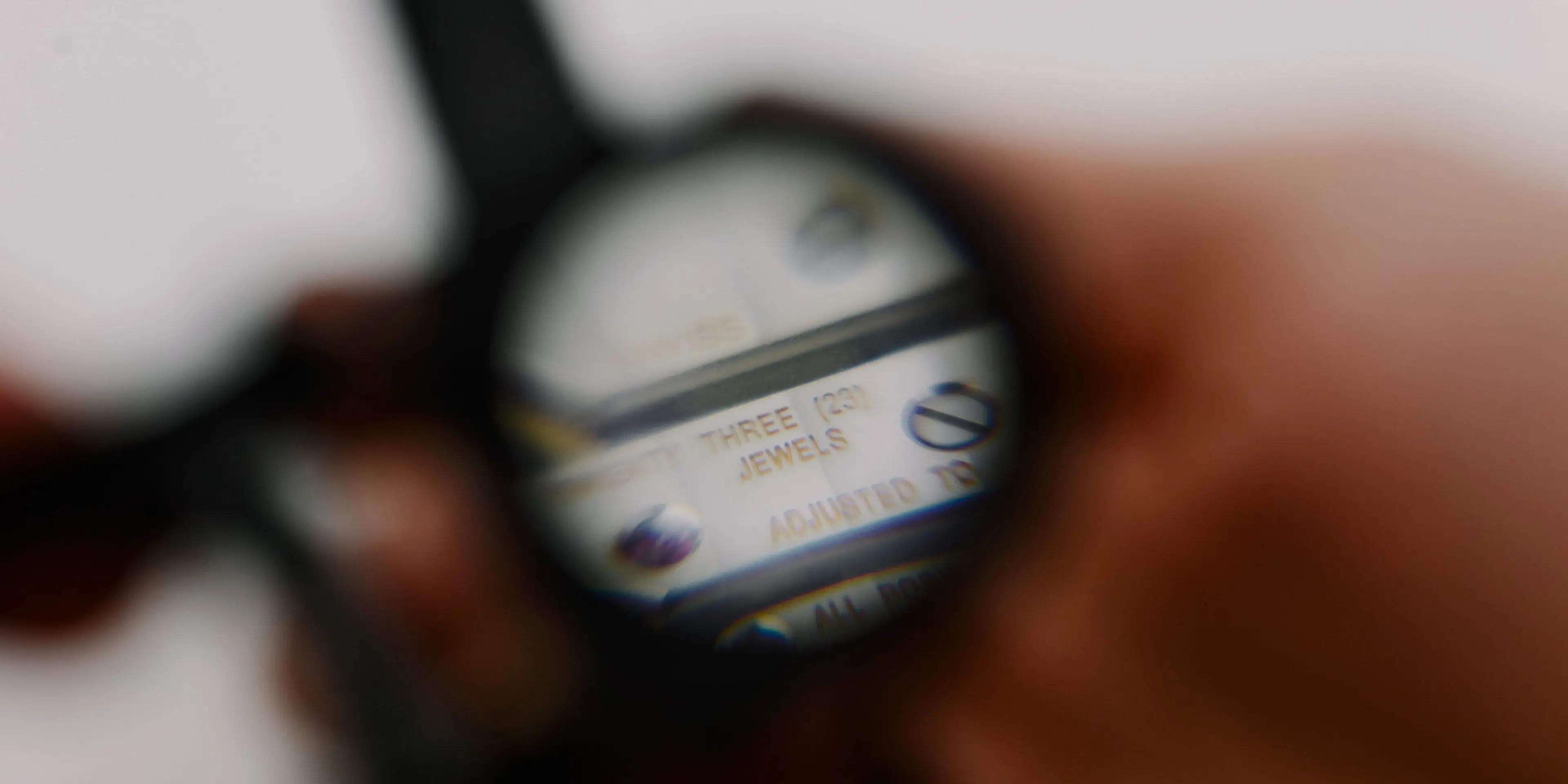 Close-up of a magnifying loupe held over a luxury watch dial, with stickers and labels just visible through the lens.