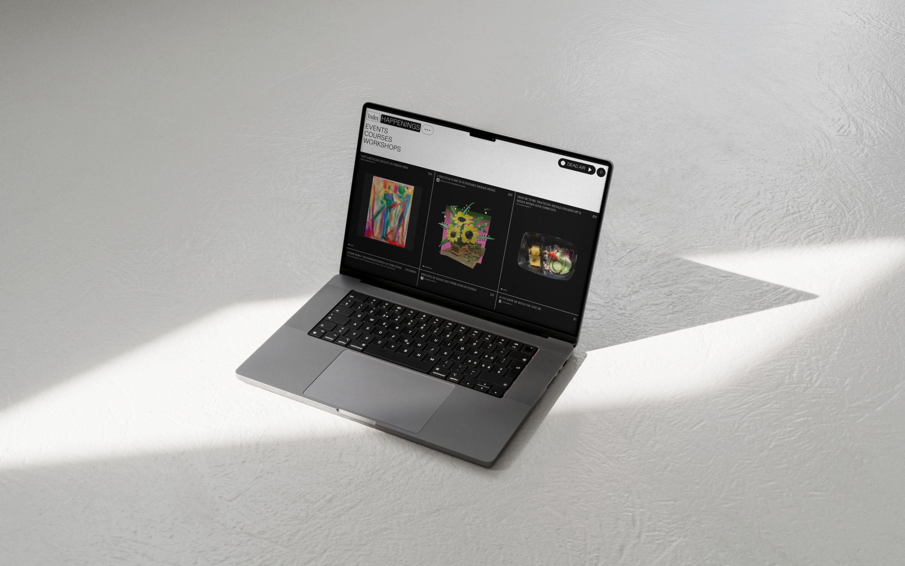 Open laptop on a white surface displaying Index radio show artwork, lit by raking daylight.