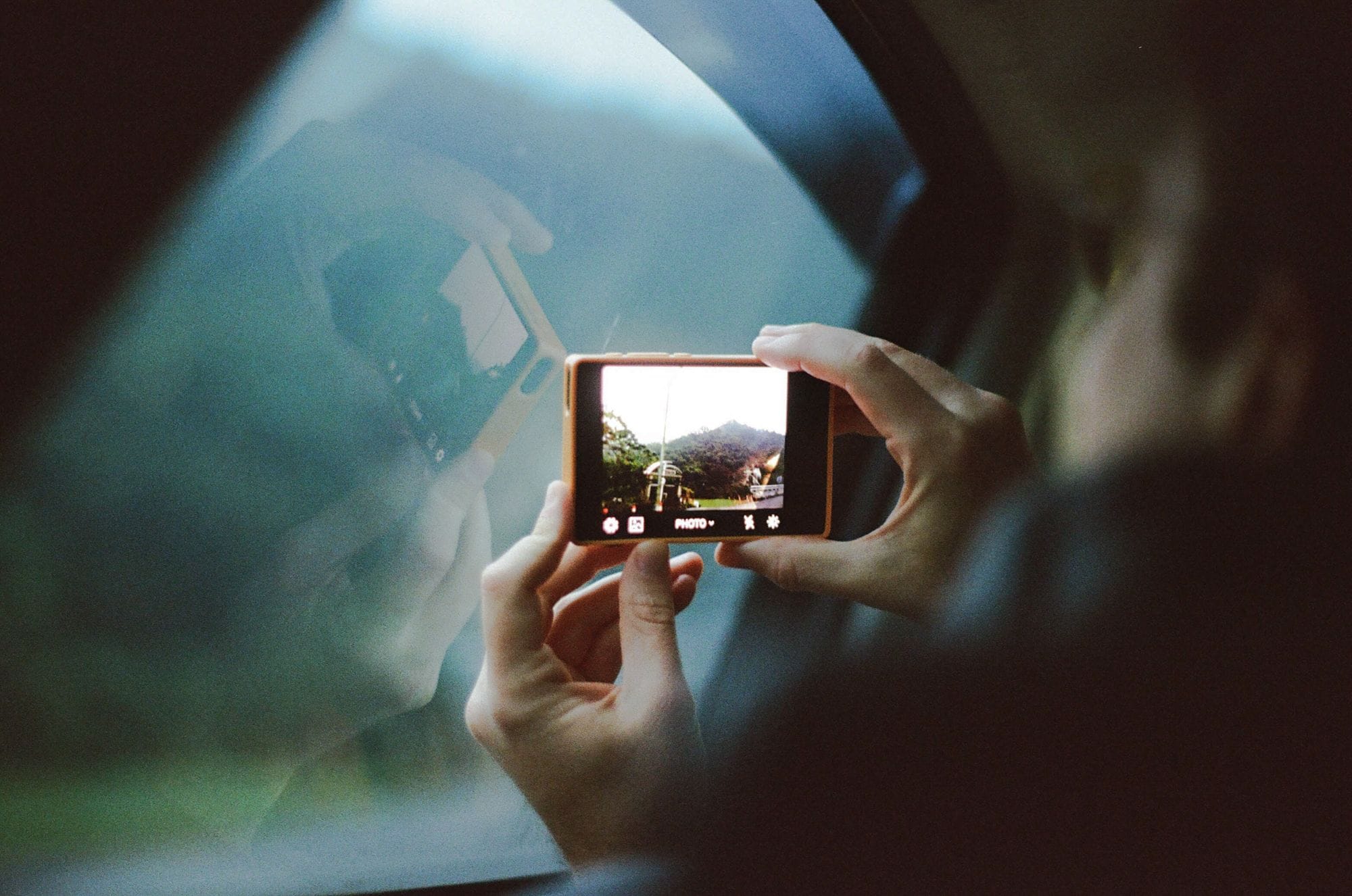 Person framing a landscape shot through a car window on a Light Phone III, with mountains visible through the windshield.