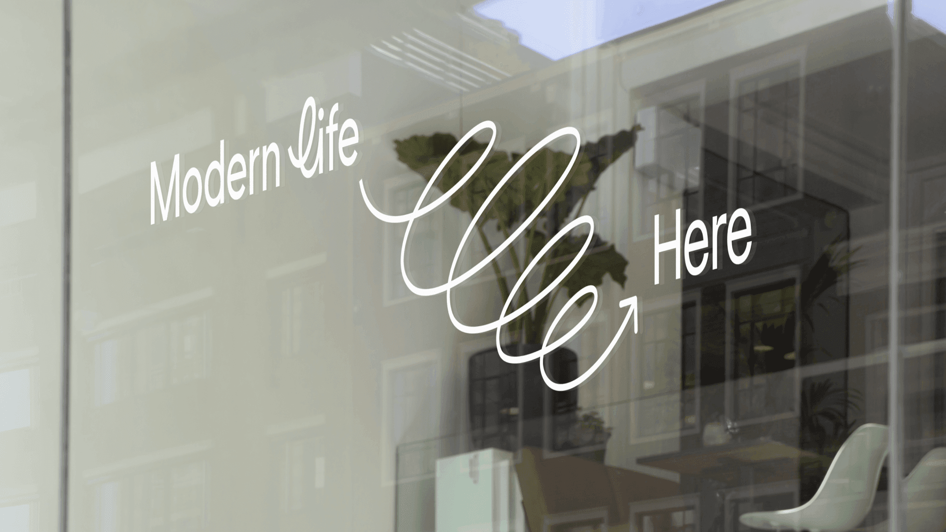 Storefront window decal reading ‘Modern Life Here’, with the brand’s script wordmark and curved arrow flourish.