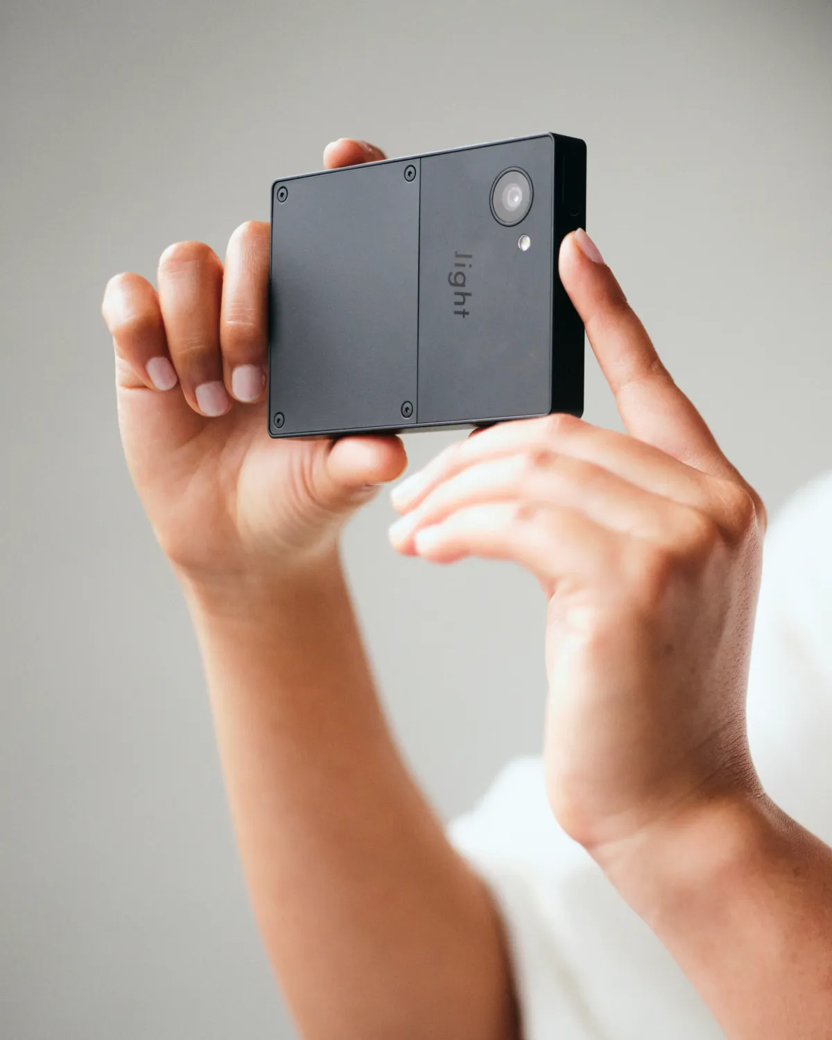 A person holding a Light Phone III in both hands, framing a photo with its rear camera.