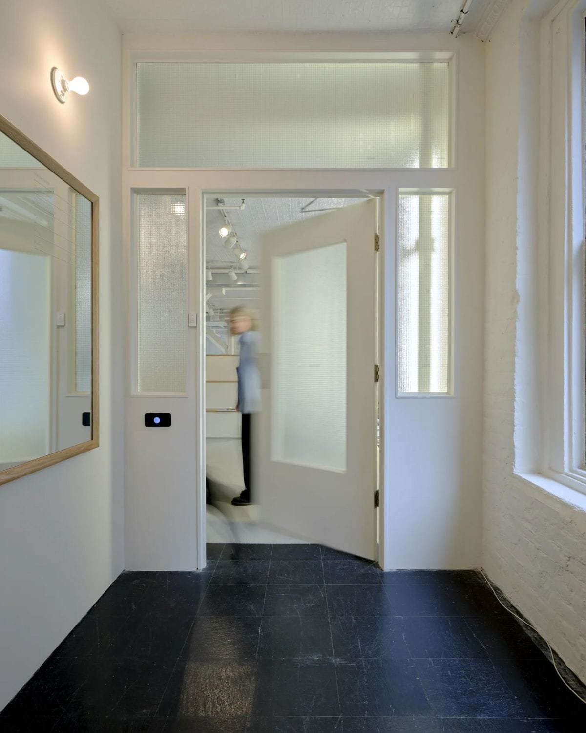 Photograph of a person stepping through a doorway into the Index studio entry, with black flooring and white walls.