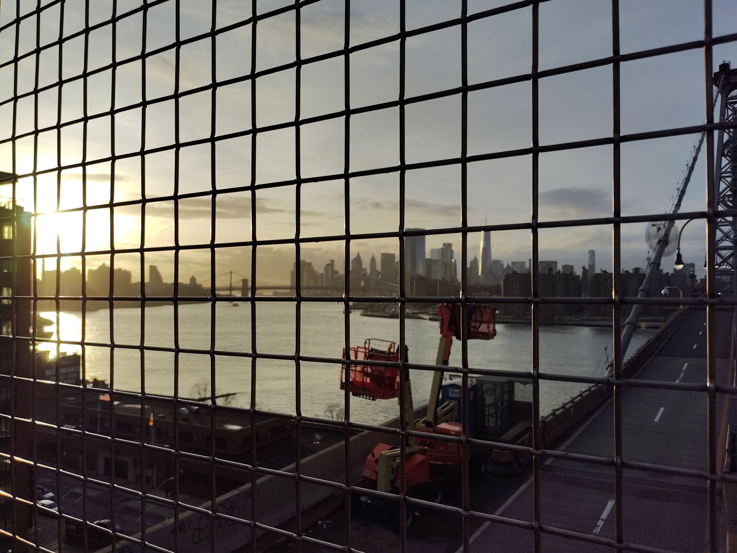 Sunset reflected through a grid of windows looking out across a river toward a city skyline, photographed on a Light Phone III.