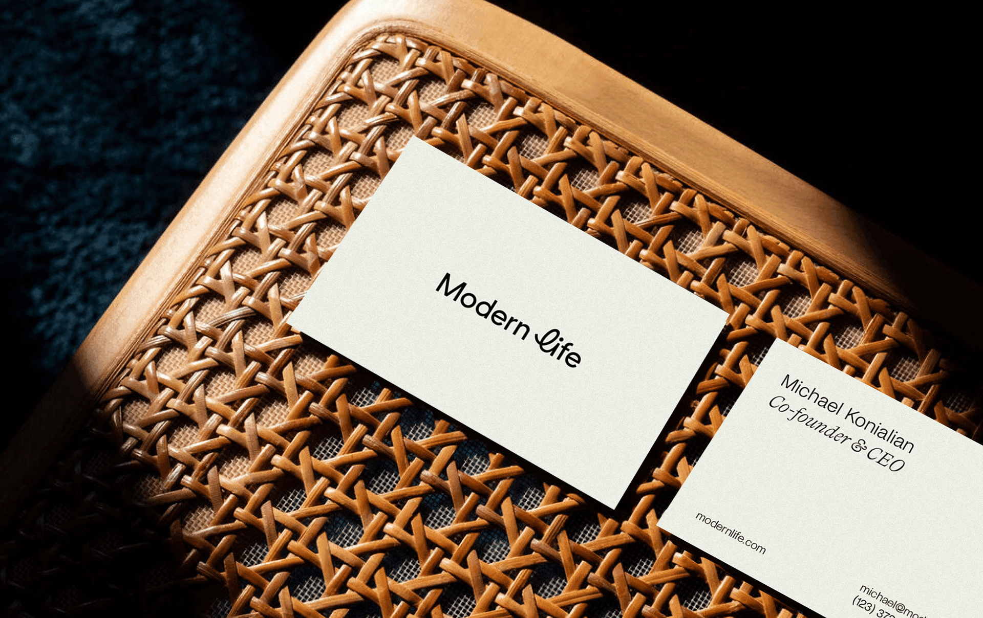 Modern Life business cards on a rattan tray, one printed with the brand wordmark and one with an advisor’s contact details.